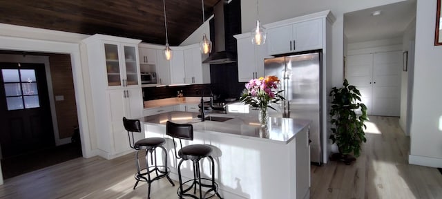 kitchen featuring wall chimney exhaust hood, appliances with stainless steel finishes, light wood-style floors, and lofted ceiling