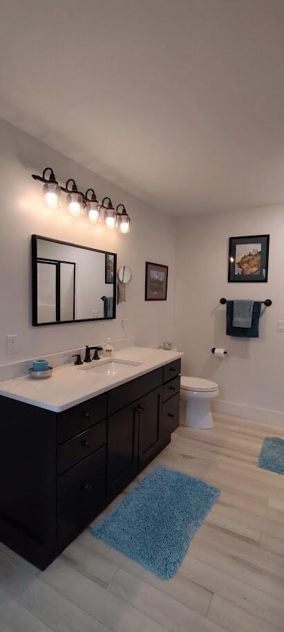 bathroom with toilet, vanity, wood finished floors, and baseboards