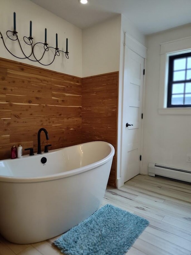 bathroom featuring recessed lighting, a freestanding tub, wood finished floors, wooden walls, and a baseboard radiator