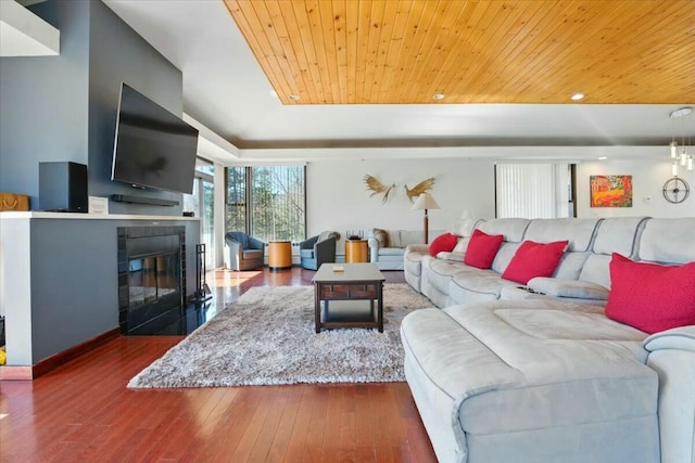 living area with wood ceiling, a tile fireplace, a tray ceiling, and hardwood / wood-style floors