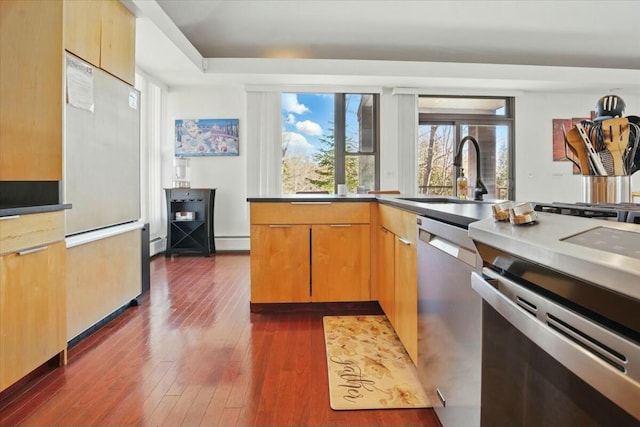 kitchen featuring a baseboard heating unit, dark wood-style floors, stainless steel appliances, and a sink