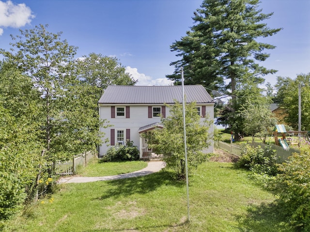 colonial-style house with fence, metal roof, a front lawn, and a playground