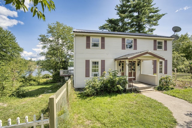 colonial house featuring fence private yard, a porch, a front yard, and metal roof