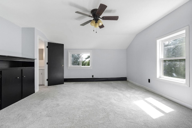 additional living space featuring light colored carpet, a ceiling fan, lofted ceiling, and baseboards