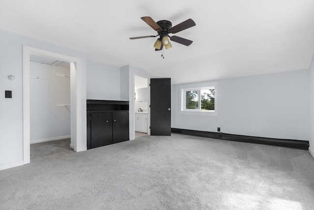 unfurnished bedroom with baseboards, carpet, a ceiling fan, ensuite bath, and a walk in closet