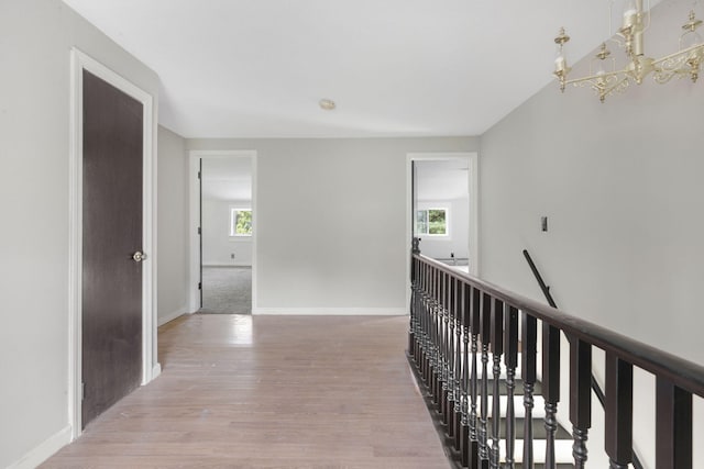 corridor featuring light wood finished floors, an upstairs landing, a chandelier, and baseboards