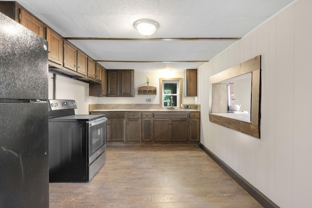 kitchen featuring stainless steel range with electric stovetop, freestanding refrigerator, hardwood / wood-style flooring, and light countertops