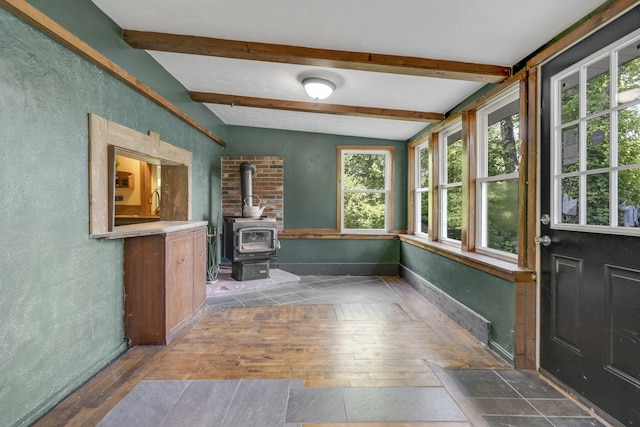 unfurnished sunroom with a wood stove, vaulted ceiling with beams, a healthy amount of sunlight, and wood-type flooring