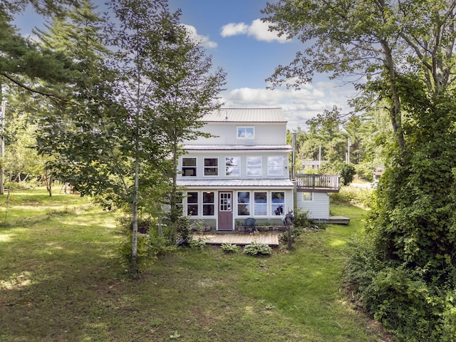 back of property featuring a wooden deck, a balcony, metal roof, and a lawn