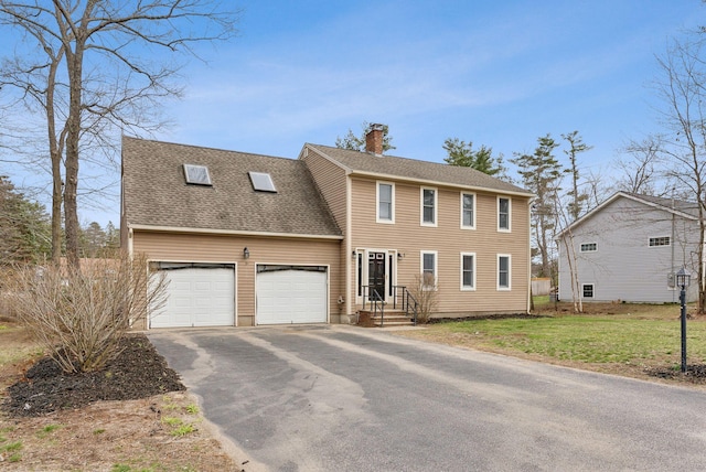 colonial inspired home with a chimney, a front lawn, driveway, a garage, and roof with shingles