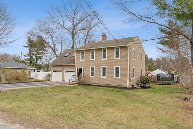 colonial-style house with a trampoline, a chimney, driveway, fence, and a front yard