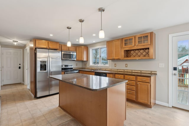 kitchen with stainless steel appliances, dark stone countertops, a center island, baseboards, and glass insert cabinets