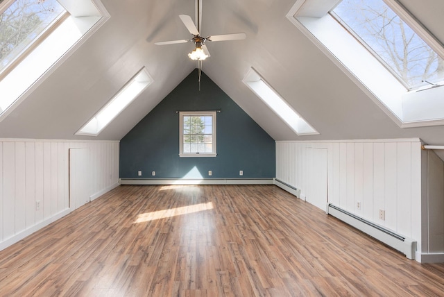additional living space with a baseboard heating unit, lofted ceiling with skylight, baseboard heating, wood finished floors, and ceiling fan