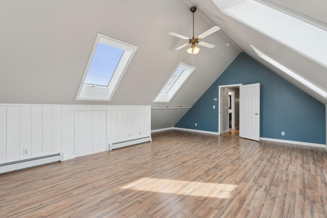 additional living space with baseboard heating, lofted ceiling with skylight, a ceiling fan, and wood finished floors