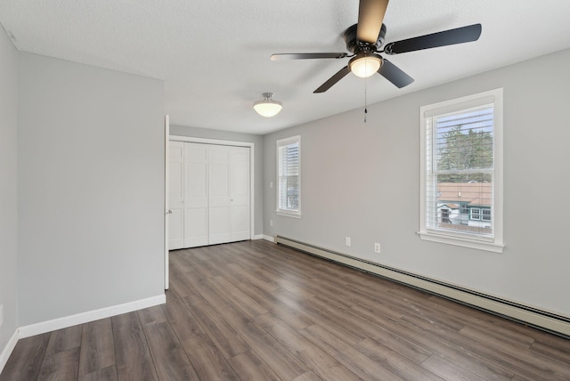 unfurnished bedroom featuring baseboard heating, wood finished floors, a closet, and multiple windows