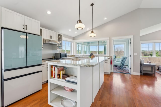 kitchen with open shelves, stainless steel microwave, built in fridge, light stone counters, and a sink