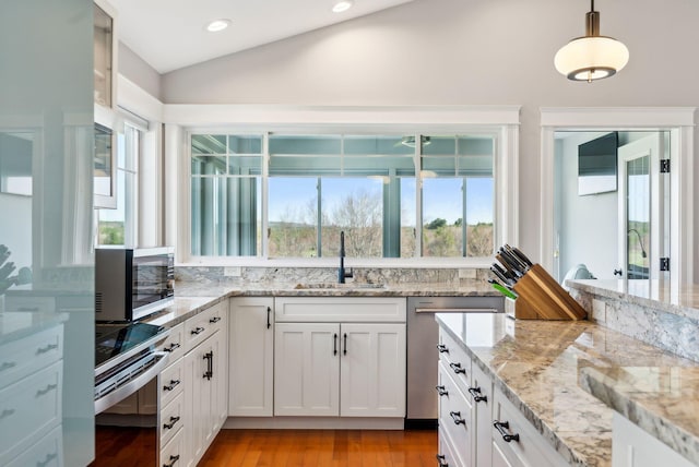 kitchen with a sink, appliances with stainless steel finishes, vaulted ceiling, and white cabinetry