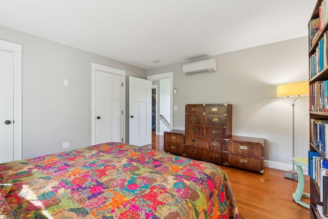bedroom with wood finished floors, baseboards, and a wall mounted AC