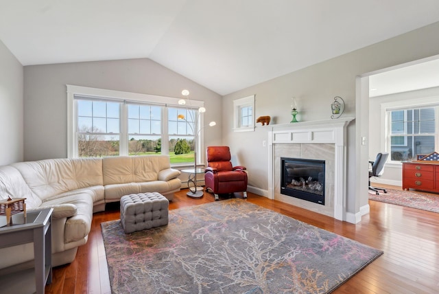 living area with a tiled fireplace, a baseboard radiator, vaulted ceiling, and wood finished floors