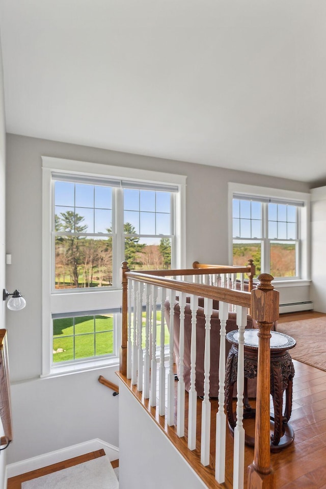 stairway featuring baseboards, a baseboard heating unit, and wood finished floors