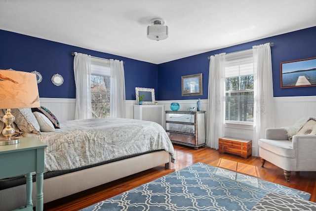 bedroom with wood finished floors, multiple windows, and wainscoting