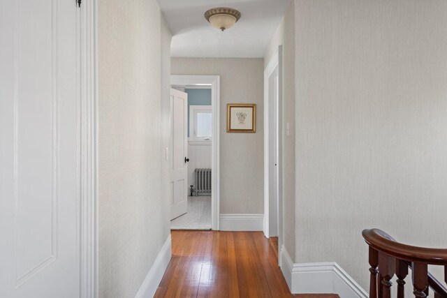 corridor with hardwood / wood-style floors, radiator heating unit, and baseboards
