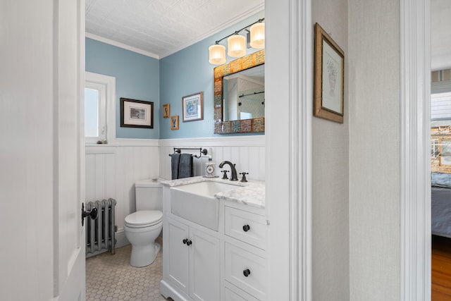 bathroom with radiator heating unit, a wainscoted wall, toilet, vanity, and ornamental molding