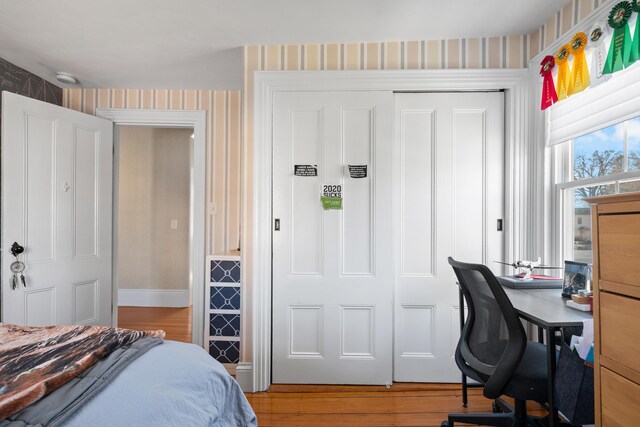 bedroom with wallpapered walls, wood finished floors, a closet, and baseboards