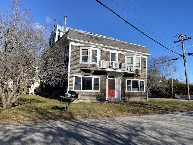 view of front of property with a shingled roof, a balcony, and a front yard
