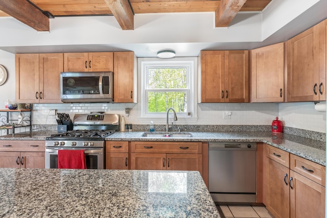 kitchen featuring appliances with stainless steel finishes, a sink, beamed ceiling, dark stone counters, and tasteful backsplash
