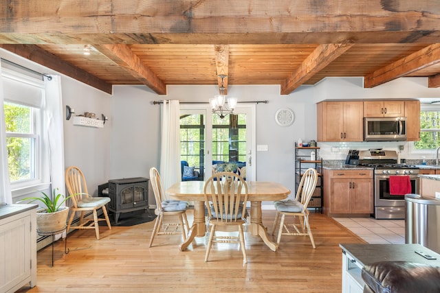 dining space with beam ceiling, wood ceiling, a chandelier, light wood-style flooring, and a wood stove
