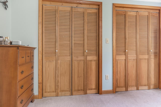 bedroom featuring light colored carpet, multiple closets, and baseboards