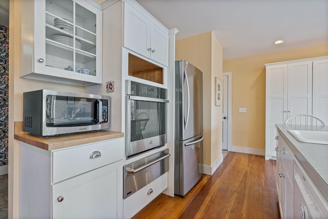 18 Pleasant St, Newcastle, ME 04553 - kitchen featuring appliances with stainless steel finishes, a warming drawer, hardwood / wood-style floors, white cabinetry, and glass insert cabinets