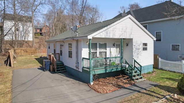 bungalow with a porch, a front lawn, fence, and a shingled roof