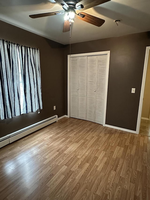 unfurnished bedroom with baseboards, baseboard heating, wood finished floors, a closet, and ceiling fan