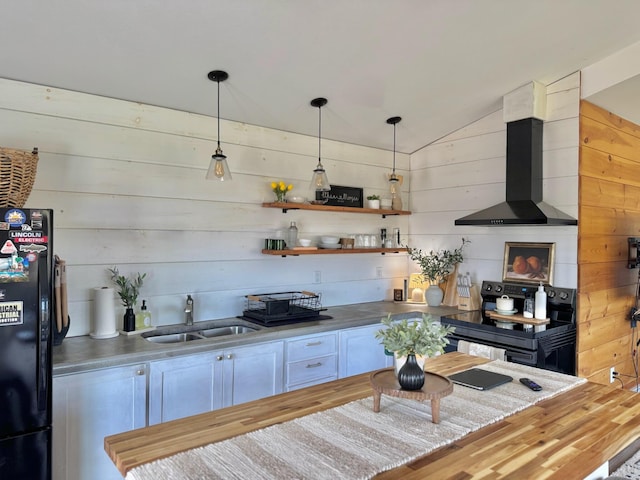 kitchen with wall chimney range hood, vaulted ceiling, wooden counters, black appliances, and a sink