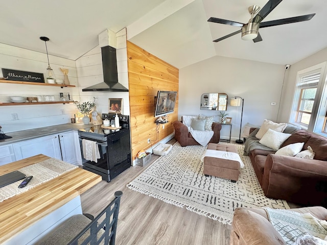 living area with wooden walls, light wood finished floors, a ceiling fan, and vaulted ceiling