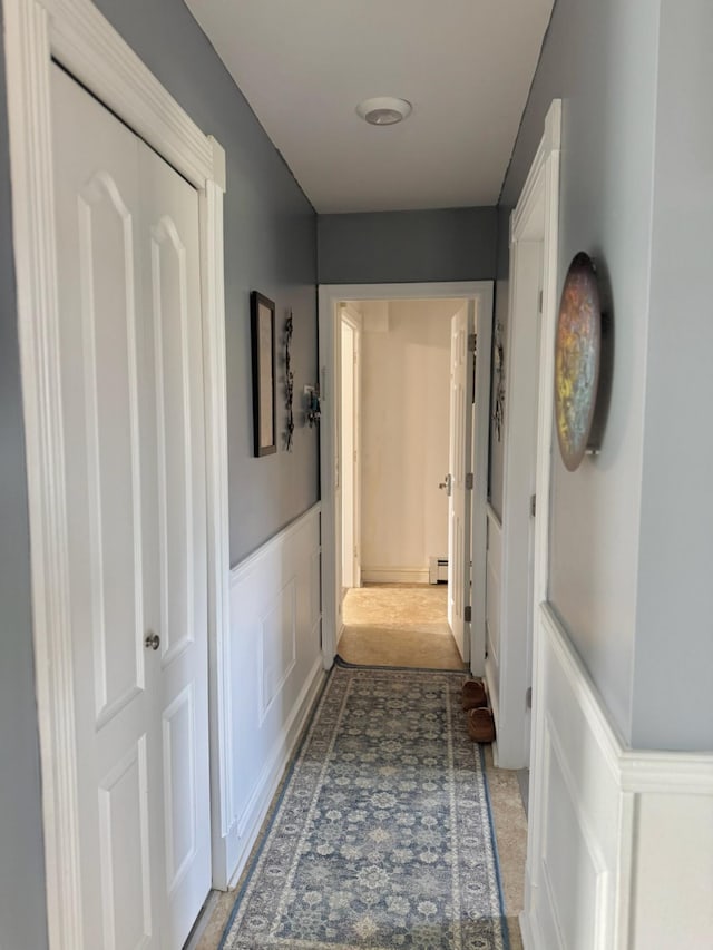 corridor featuring a wainscoted wall, baseboard heating, and a decorative wall