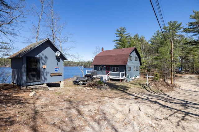 exterior space with a gambrel roof, roof with shingles, and a chimney