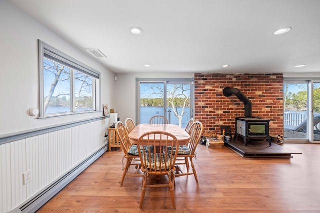dining area featuring a wood stove, visible vents, light wood-style flooring, recessed lighting, and a baseboard heating unit
