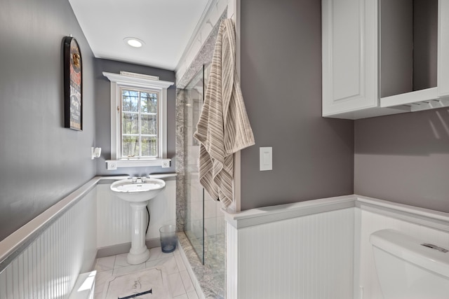 bathroom featuring toilet, walk in shower, and wainscoting