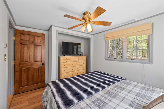 bedroom with crown molding, ceiling fan, wood finished floors, and visible vents