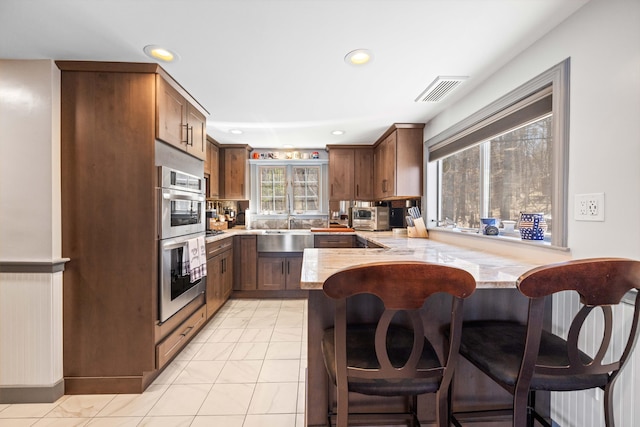 kitchen with a breakfast bar area, visible vents, double oven, a peninsula, and recessed lighting