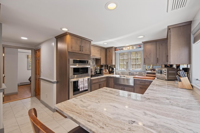 kitchen featuring a sink, stainless steel double oven, light stone countertops, and a toaster