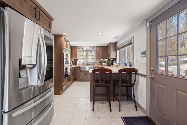 kitchen with visible vents, a peninsula, a breakfast bar area, light countertops, and stainless steel appliances