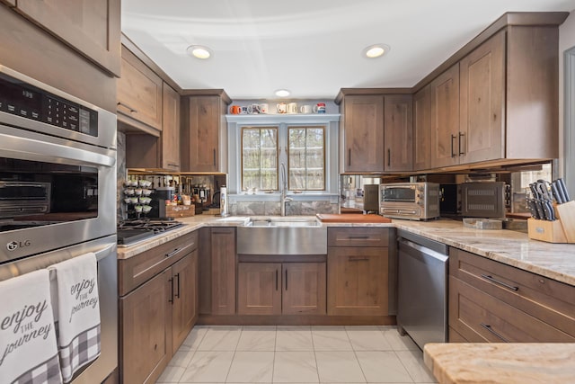kitchen featuring light stone counters, a sink, marble finish floor, stainless steel appliances, and a toaster