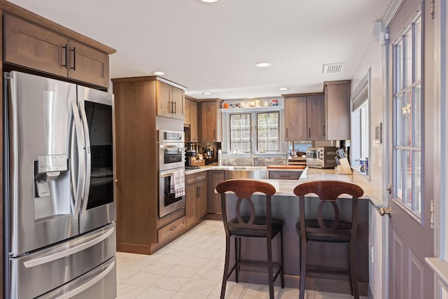 kitchen featuring visible vents, a peninsula, a breakfast bar, stainless steel appliances, and recessed lighting