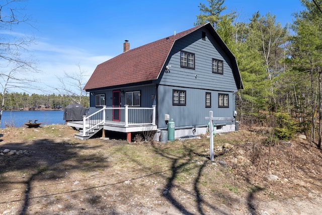 exterior space featuring a water view, a gambrel roof, a chimney, and a shingled roof