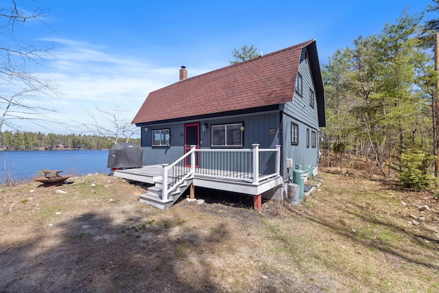 view of front of house with a shingled roof, a chimney, a water view, and a gambrel roof
