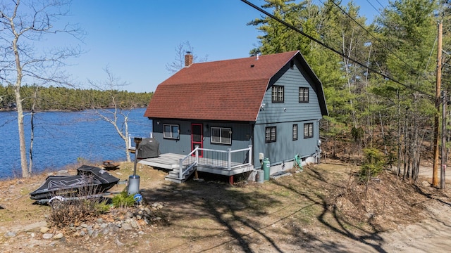exterior space featuring a water view, a chimney, a gambrel roof, and a wooded view
